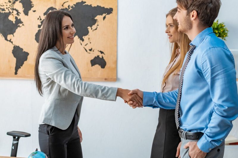 Travel Agent shaking hands with young couple after using her CRM